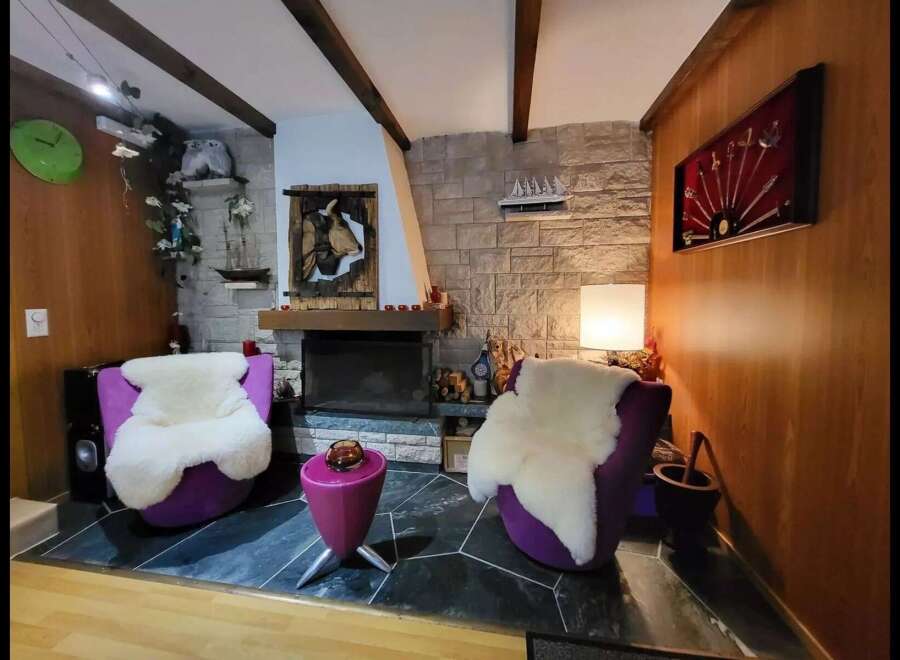 Cozy living room featuring two plush purple armchairs with fluffy white sheepskin throws, centered around a stone fireplace.