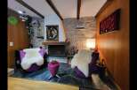 Cozy living room featuring two plush purple armchairs with fluffy white sheepskin throws, centered around a stone fireplace.