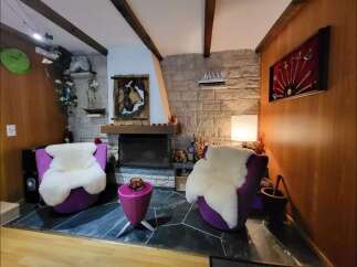 Cozy living room featuring two plush purple armchairs with fluffy white sheepskin throws, centered around a stone fireplace.