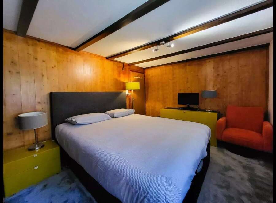 Experience cozy comfort in this charming bedroom, featuring warm wood-paneled walls and exposed beam ceilings.