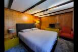 Experience cozy comfort in this charming bedroom, featuring warm wood-paneled walls and exposed beam ceilings.