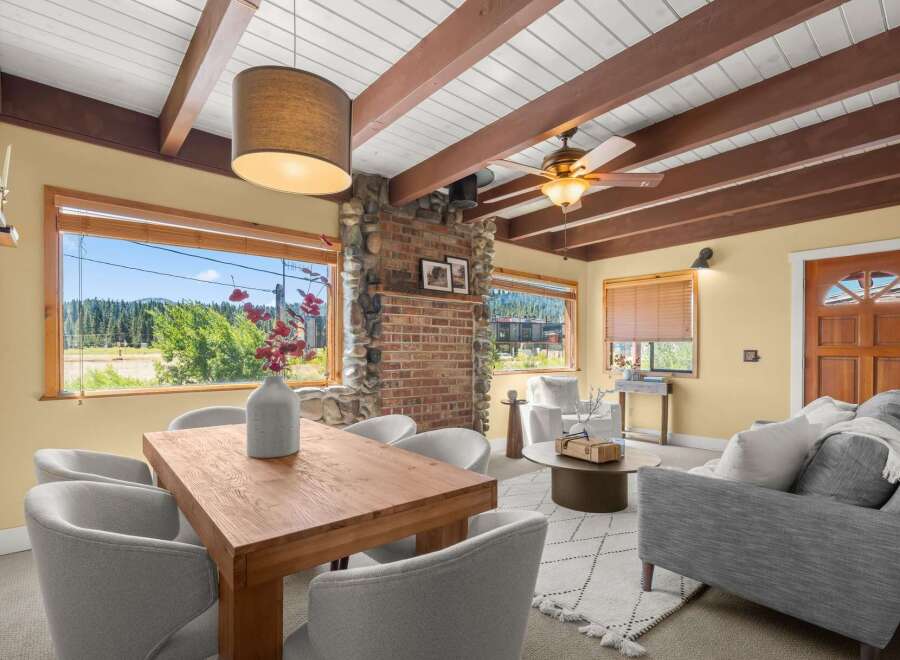 Experience breathtaking mountain views from this charming living and dining area, featuring a cozy brick fireplace and exposed wooden beams.