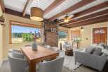 Experience breathtaking mountain views from this charming living and dining area, featuring a cozy brick fireplace and exposed wooden beams.