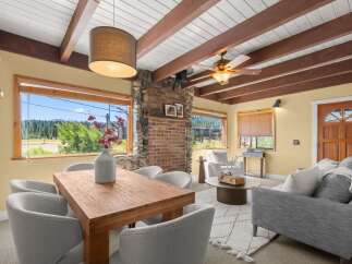 Experience breathtaking mountain views from this charming living and dining area, featuring a cozy brick fireplace and exposed wooden beams.