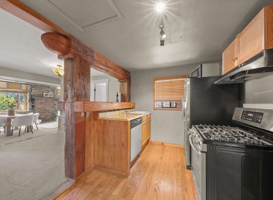 Discover a charming kitchen featuring rustic wooden beams and cabinetry, complemented by a stainless steel gas range and dishwasher.