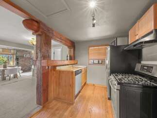 Discover a charming kitchen featuring rustic wooden beams and cabinetry, complemented by a stainless steel gas range and dishwasher.