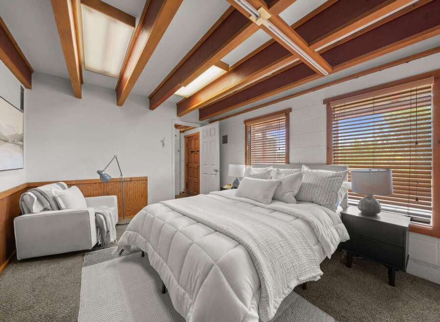 Discover this charming bedroom featuring a cozy queen-size bed adorned with plush white bedding and a textured throw.