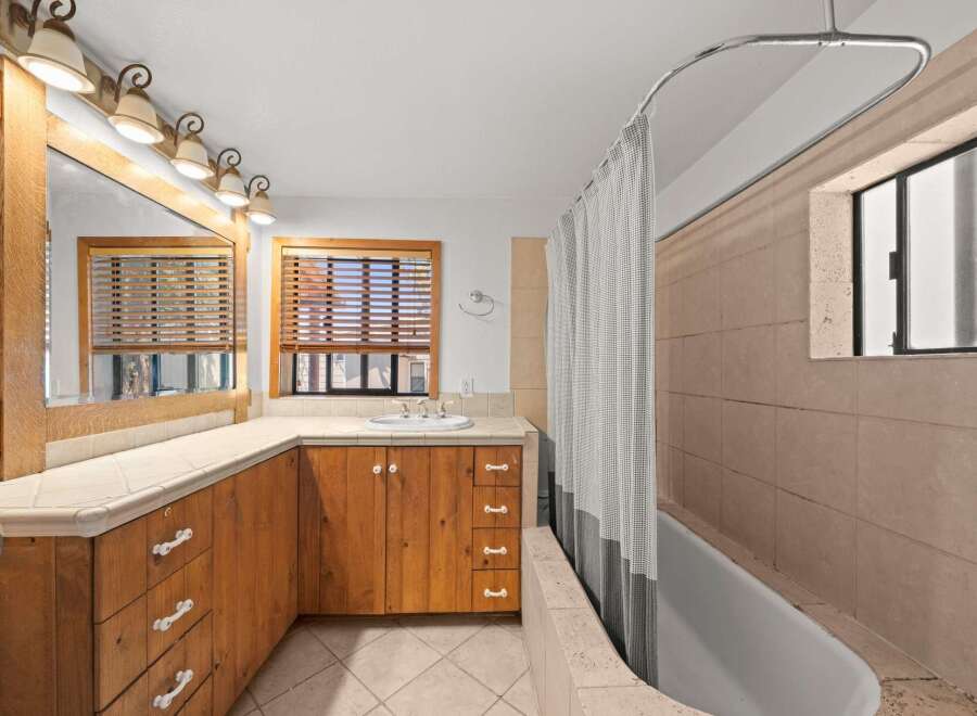 This charming bathroom features a spacious vanity with ample storage, complemented by a large mirror and a row of elegant sconce lighting.