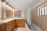 This charming bathroom features a spacious vanity with ample storage, complemented by a large mirror and a row of elegant sconce lighting.