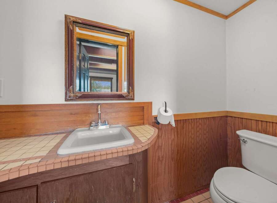 This charming bathroom features a classic white sink set against a warm wooden vanity and tiled countertop.