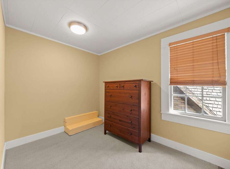 This bedroom features a warm and inviting atmosphere with its soft yellow walls and neutral carpeting.