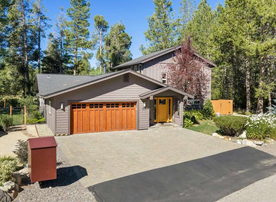 Discover this charming home featuring a warm and inviting ambiance, highlighted by a beautiful wooden garage door and a bright yellow front door.