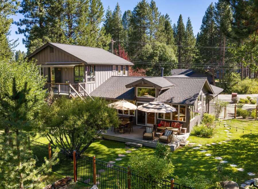 This charming home offers a spacious deck perfect for outdoor entertaining, complete with comfortable seating and dining areas under umbrellas.