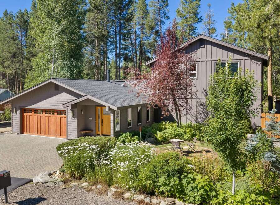 Nestled among tall pines, this charming home offers a serene retreat with its inviting facade and lush landscaping.