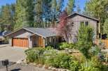 Nestled among tall pines, this charming home offers a serene retreat with its inviting facade and lush landscaping.