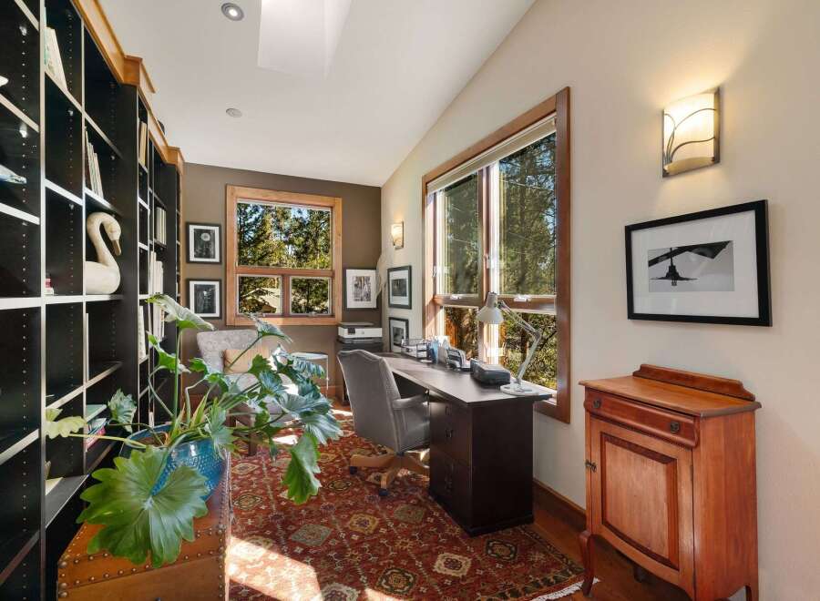 This home office offers a serene and productive environment with ample natural light streaming through large windows overlooking a wooded landscape.