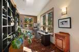 This home office offers a serene and productive environment with ample natural light streaming through large windows overlooking a wooded landscape.