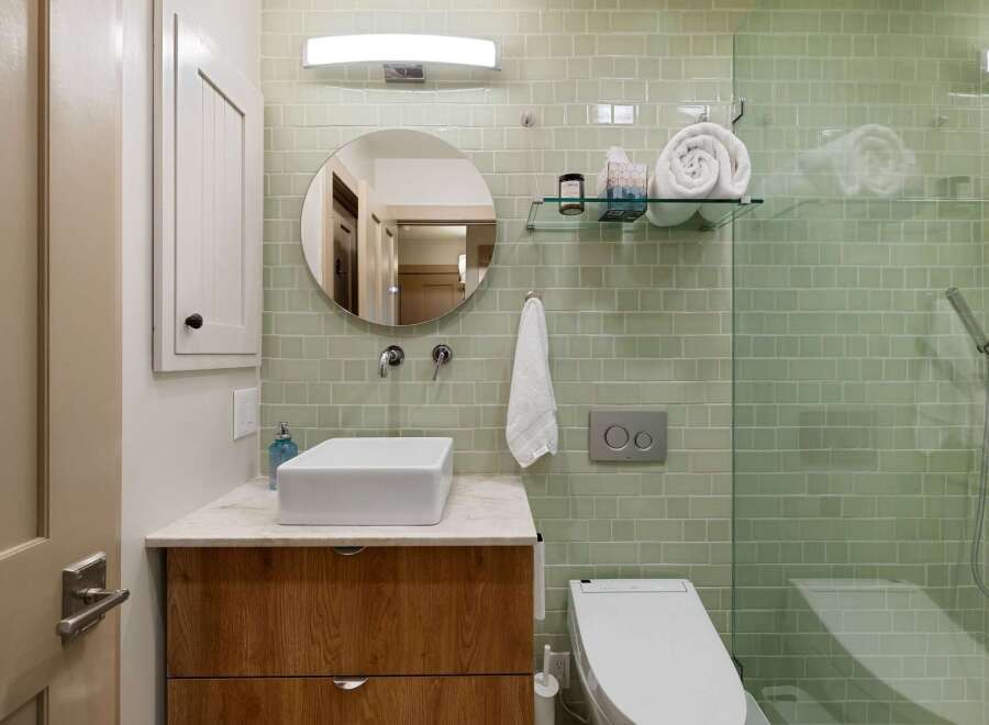 This modern bathroom features a sleek design with light green subway tile walls and a floating wood vanity.