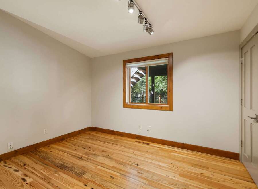 This empty room features beautiful natural light streaming in through a large window, highlighting the warm tones of the hardwood floors.