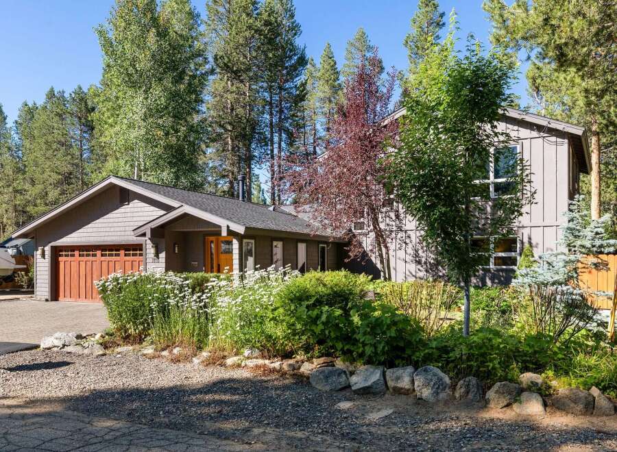 Discover this charming home nestled among mature trees, featuring a welcoming entryway and a spacious garage with a beautiful wood-paneled door.