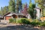 Discover this charming home nestled among mature trees, featuring a welcoming entryway and a spacious garage with a beautiful wood-paneled door.
