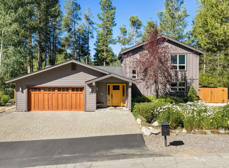 Discover this charming home nestled among tall pine trees, featuring a warm wooden garage door and a vibrant yellow front door that welcomes you in.