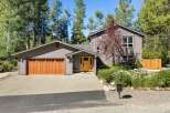 Discover this charming home nestled among tall pine trees, featuring a warm wooden garage door and a vibrant yellow front door that welcomes you in.