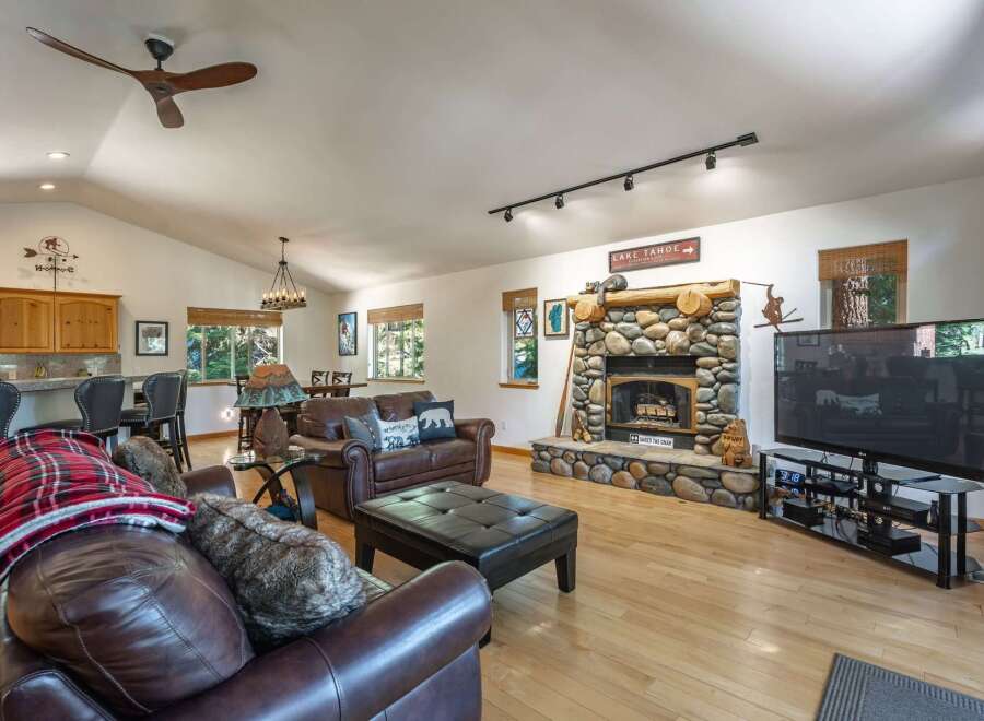 Experience rustic charm in this spacious living area, featuring a grand stone fireplace and a vaulted ceiling with a modern fan.