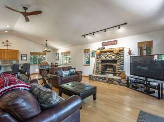 Experience rustic charm in this spacious living area, featuring a grand stone fireplace and a vaulted ceiling with a modern fan.