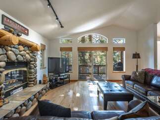 Experience the ultimate mountain retreat in this stunning living room, featuring a grand stone fireplace and a rustic log mantle.