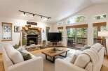 Experience the ultimate mountain retreat in this stunning living room, featuring a grand stone fireplace and vaulted ceilings with large windows that offer breathtaking forest views.