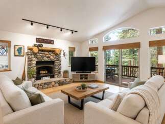 Experience the ultimate mountain retreat in this stunning living room, featuring a grand stone fireplace and vaulted ceilings with large windows that offer breathtaking forest views.