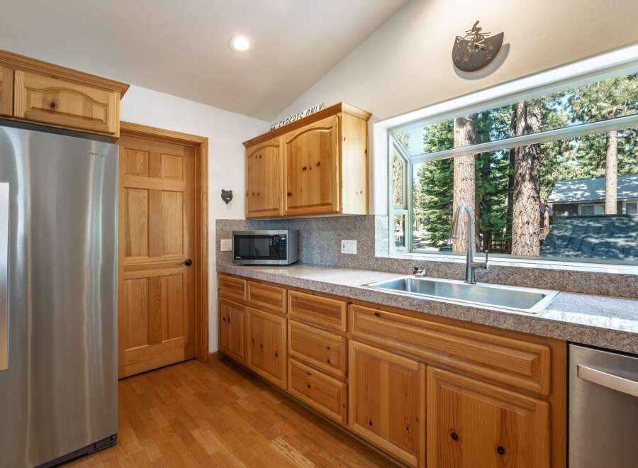 This charming kitchen boasts beautiful natural wood cabinetry and a large window offering picturesque views of surrounding trees.