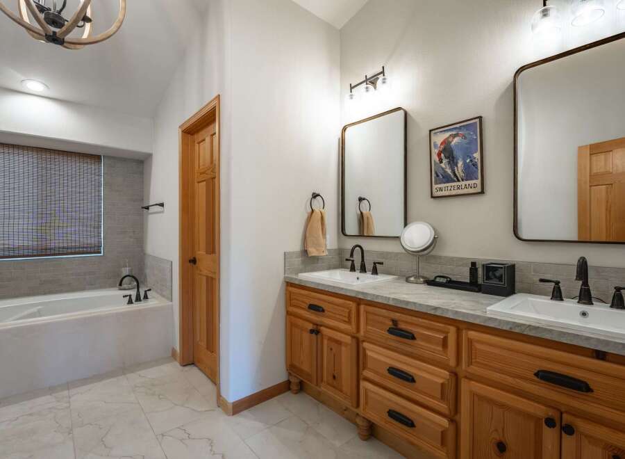 This spacious bathroom features a deep soaking tub with a tiled surround and a bamboo blind for privacy.