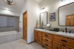 This spacious bathroom features a deep soaking tub with a tiled surround and a bamboo blind for privacy.