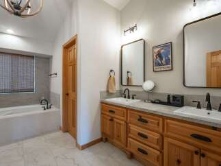 This spacious bathroom features a deep soaking tub with a tiled surround and a bamboo blind for privacy.