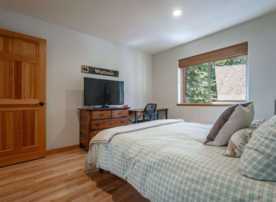 This charming bedroom features a cozy plaid comforter and a wooden dresser topped with a television.
