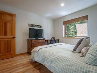 This charming bedroom features a cozy plaid comforter and a wooden dresser topped with a television.