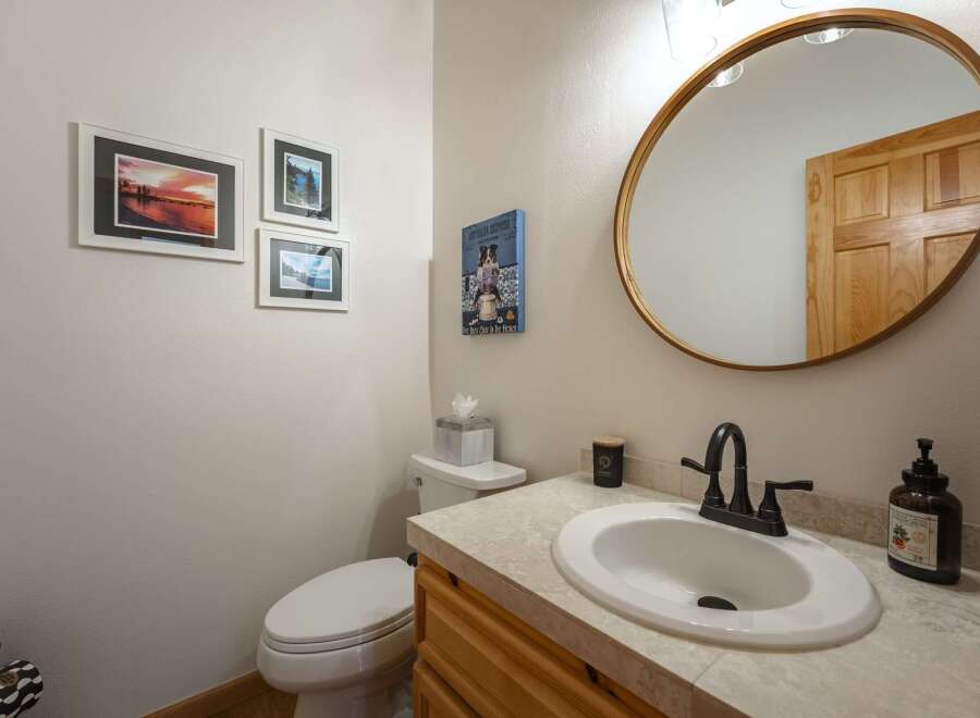 This charming bathroom features a stylish vanity with a white oval sink and a dark bronze faucet, complemented by a large round mirror with a gold frame.