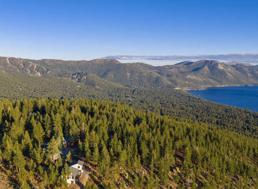 Nestled amidst a dense forest of evergreen trees, this stunning property offers breathtaking panoramic views of a serene lake and majestic mountains.
