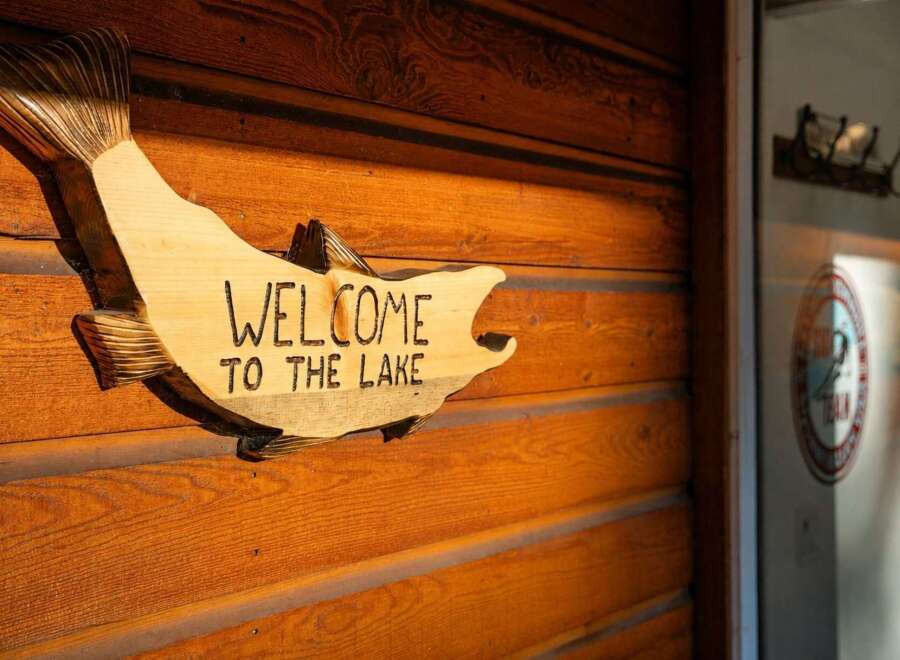 Welcome to your lakeside retreat! This charming wooden sign, shaped like a fish, reads 'WELCOME TO THE LAKE' and is mounted on a rustic wooden wall.