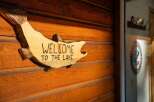 Welcome to your lakeside retreat! This charming wooden sign, shaped like a fish, reads 'WELCOME TO THE LAKE' and is mounted on a rustic wooden wall.