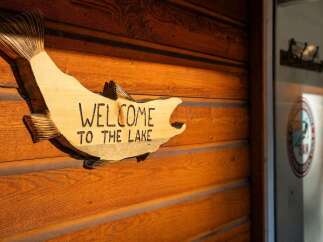 Welcome to your lakeside retreat! This charming wooden sign, shaped like a fish, reads 'WELCOME TO THE LAKE' and is mounted on a rustic wooden wall.