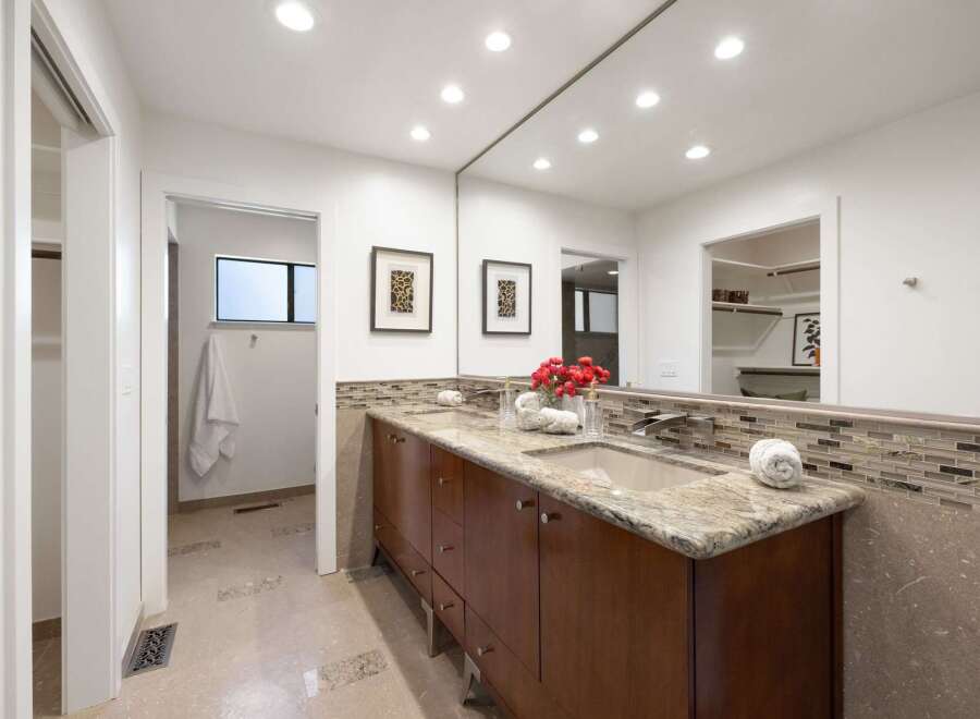 This spacious bathroom features a double vanity with granite countertops and a modern mosaic tile backsplash.