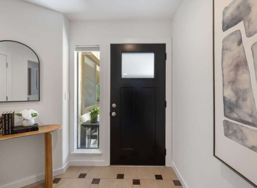 Step into this inviting entryway featuring a sleek black front door with a frosted glass window, complemented by a modern arched mirror and a charming wooden console table.