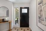 Step into this inviting entryway featuring a sleek black front door with a frosted glass window, complemented by a modern arched mirror and a charming wooden console table.
