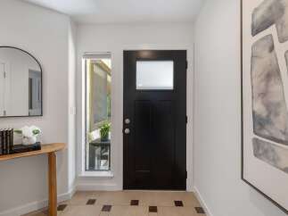 Step into this inviting entryway featuring a sleek black front door with a frosted glass window, complemented by a modern arched mirror and a charming wooden console table.