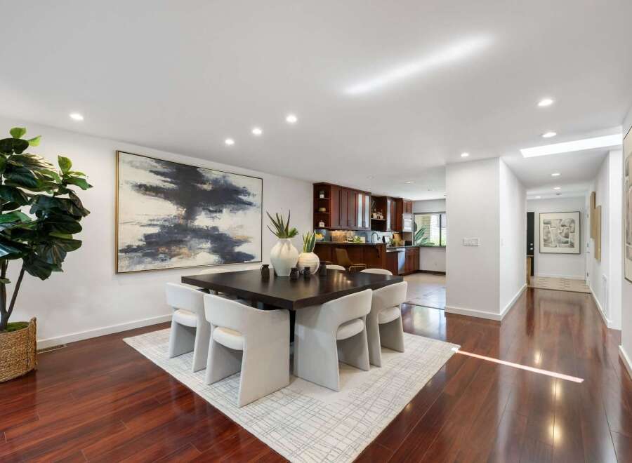 Experience elegant dining in this spacious room, featuring a large square dark wood table surrounded by plush white chairs.