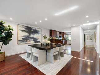 Experience elegant dining in this spacious room, featuring a large square dark wood table surrounded by plush white chairs.