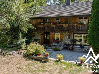Charming stone and wood chalet nestled in a lush green setting, featuring a beautiful wooden balcony adorned with flower boxes.